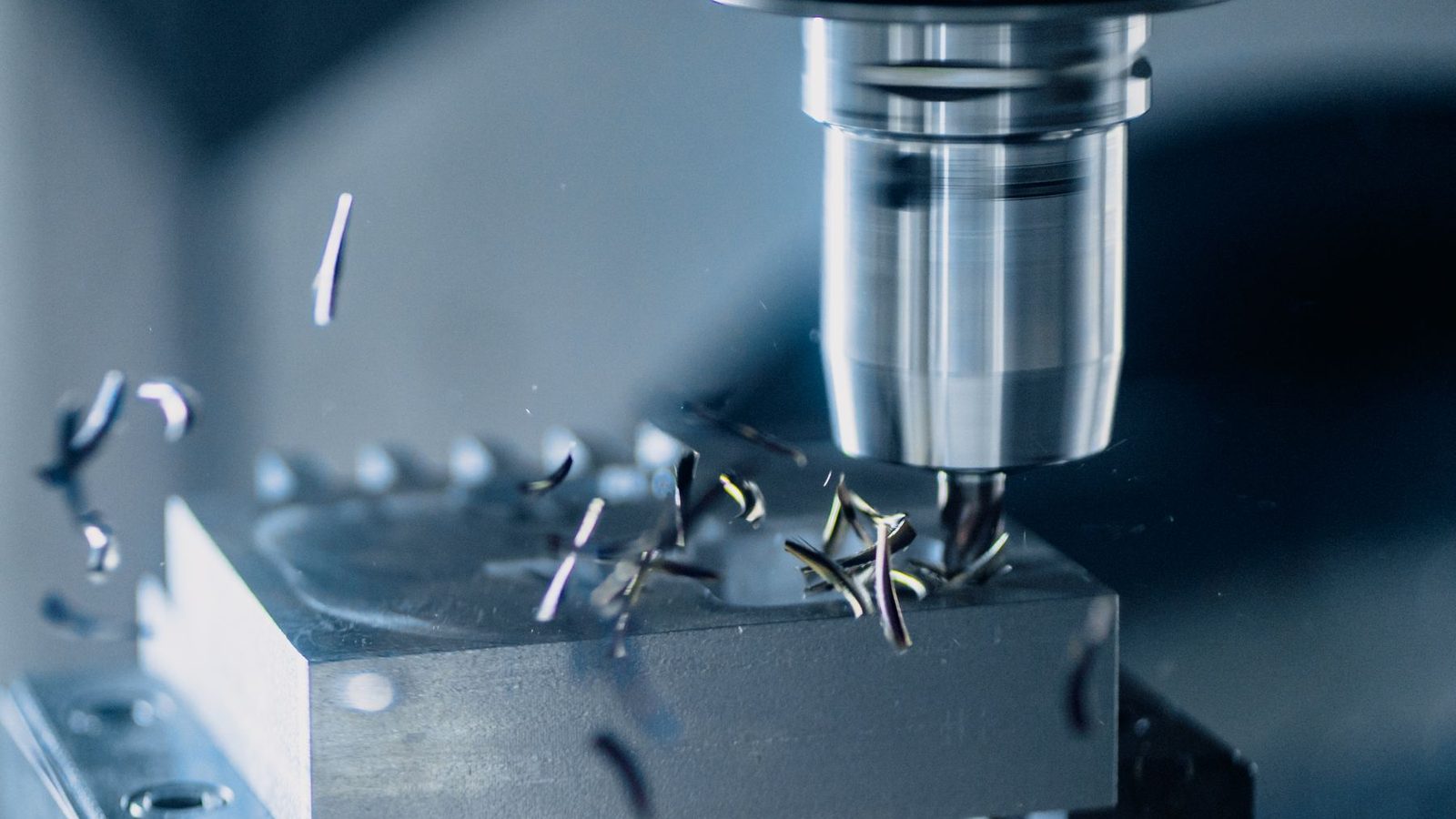 A carbide end mill cutting an aluminium block held in a vise on a CNC milling machine, chips lifting off the cut.